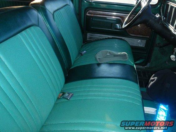 Green and black vinyl seats with seatbelts and a gray hat on the passenger seat