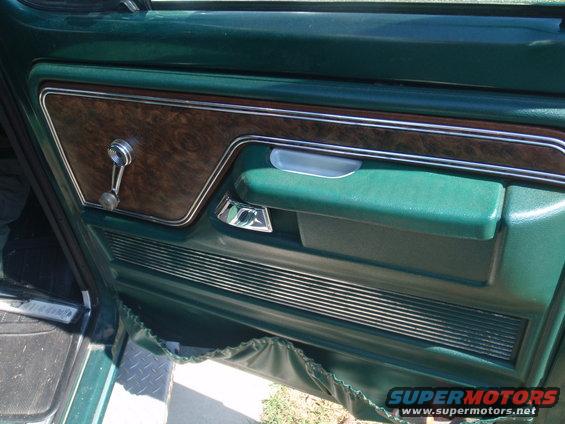 Green 1978 Ford Bronco interior door panel with woodgrain trim, chrome handle, and speaker grille