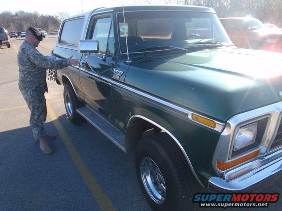 1978 Ford Bronco, green with chrome trim, parked in a lot with a person in uniform nearby