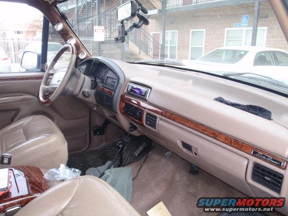 Tan interior of a 1992 Ford Bronco with wood trim, aftermarket stereo, and gauges on the A-pillar