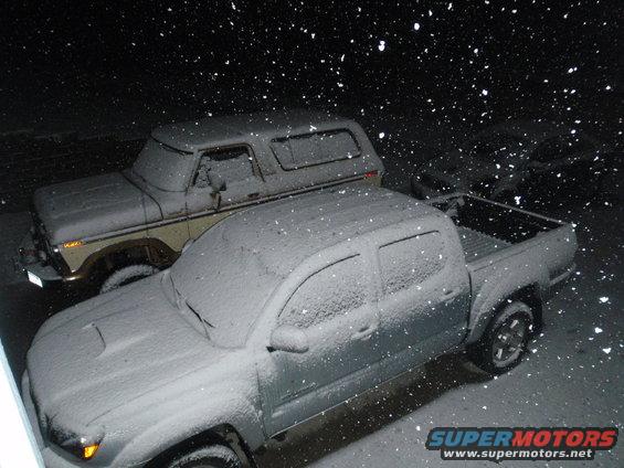 1978 Ford Bronco and a modern pickup truck covered in snow at night