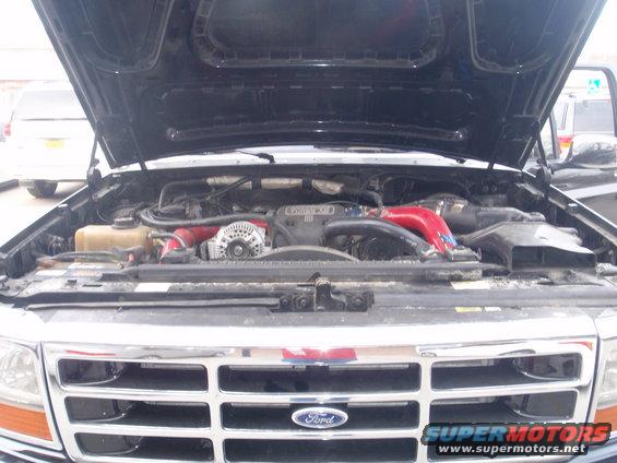 Ford truck engine bay with red intake pipes. Grille has Ford logo. Supermotors.net watermark