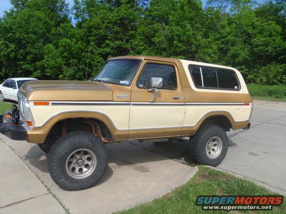 1978 Ford Bronco lifted with large tires, two-tone paint. White sedan parked behind