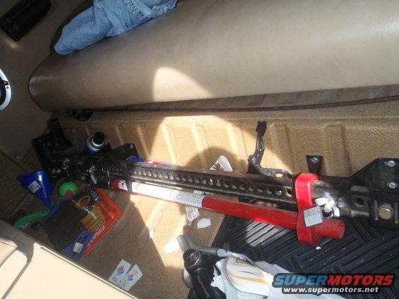 Interior view of a vehicle's cargo area with a Hi-Lift jack, blue funnel, and orange bag