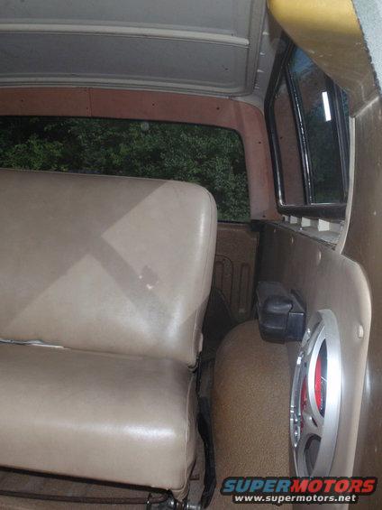 Interior shot of a vehicle showing tan seats, a speaker mounted on the side panel, and trees visible through the rear window
