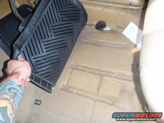 Hand removing black floor mat from tan carpeted interior