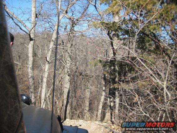 Gray Jeep Wrangler driving on a dirt path through a wooded area