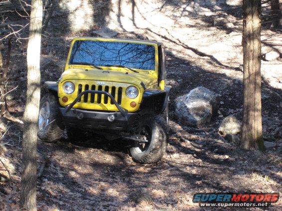 Yellow Jeep Wrangler driving on a dirt trail with trees and rocks
