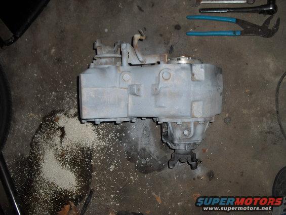 Gray transfer case on concrete floor with tools and debris