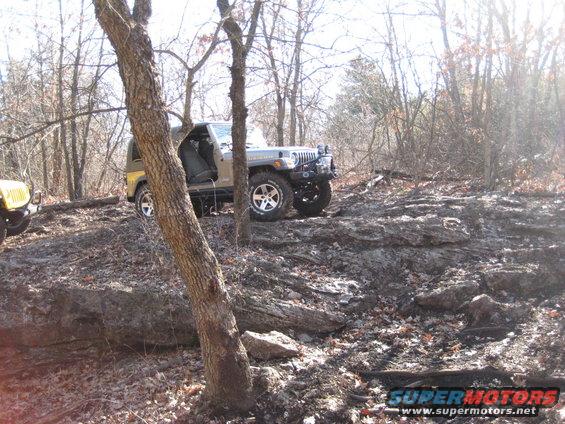 Tan Jeep Wrangler on rocky terrain, front bumper modified with off-road lights