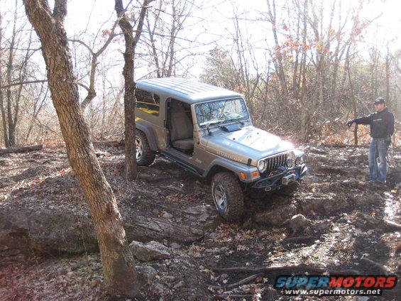 Silver 2005 Jeep Wrangler navigating rocky terrain with a person standing nearby pointing