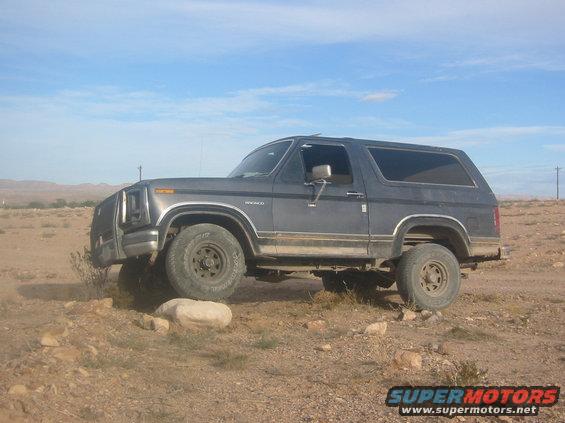 Gray Ford Bronco driving on a rocky, dirt path under a blue sky