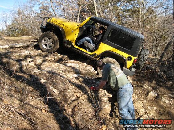 Yellow Jeep Wrangler Rubicon driving over rocks with driver inside and person outside guiding