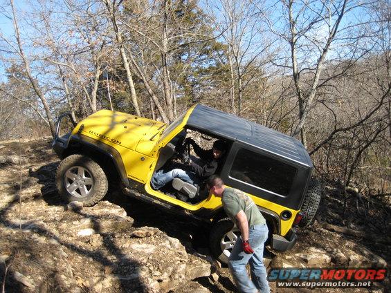 Yellow Jeep Wrangler Rubicon navigating rocky terrain with two people inside and one person outside guiding