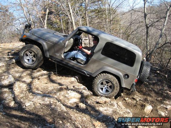 Gray 2005 Jeep Wrangler with Rubicon badging on a rocky incline, driver wearing red gloves