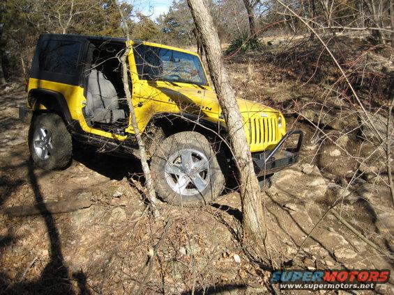 Yellow 2005 Jeep Wrangler Rubicon on a rocky trail, driver's door open, front-left tire angled up