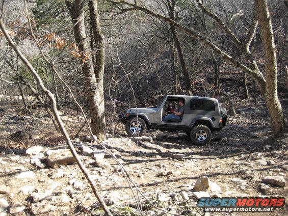 Gray 2005 Jeep Wrangler driving on a rocky, wooded trail