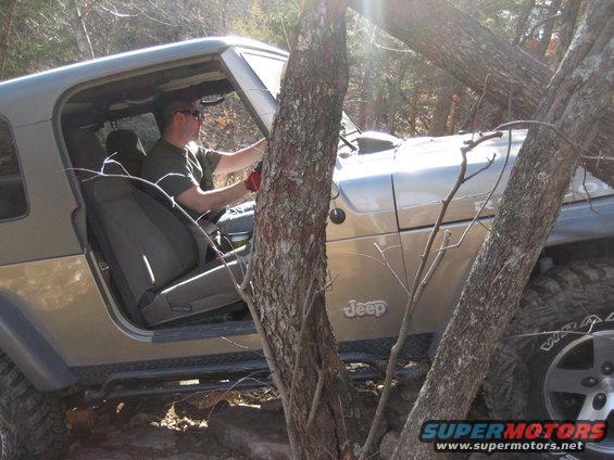 Driver in a 2005 Jeep Wrangler navigating through trees on a rocky trail