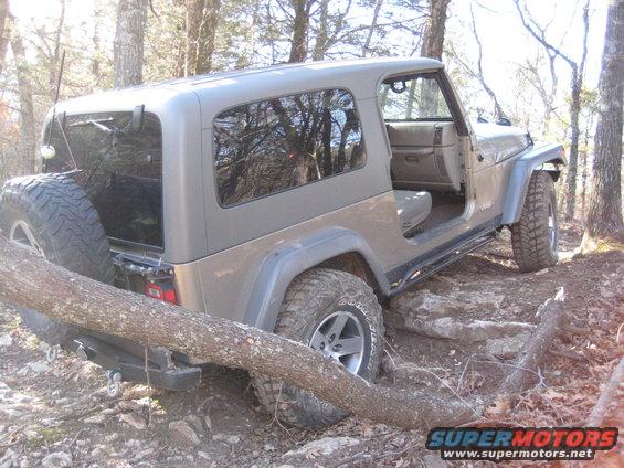 Gray Jeep Wrangler on rocky trail with fallen tree across front