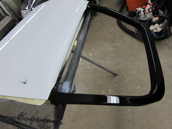 White car door with black trim on a stand, undergoing painting