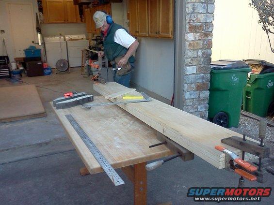 Man in garage wearing ear protection cuts wood on a workbench with a miter saw