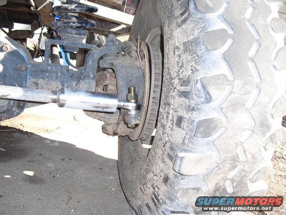 Close-up of a dirty off-road tire and suspension components, including a shock absorber and steering linkage