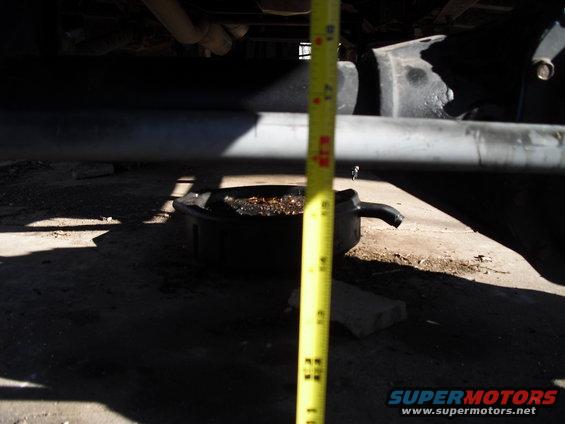 Measuring clearance under vehicle frame with a tape measure, oil pan below
