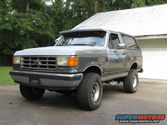 Gray Ford Bronco with a chrome grille and aftermarket wheels parked in front of a garage
