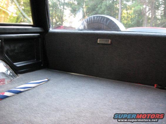 Interior cargo area of a 1988 Ford Bronco with grey carpet and a spare tire visible through the rear window