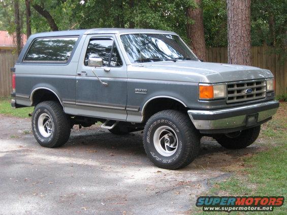 Two-tone gray 1988 Ford Bronco with aftermarket wheels parked on a gravel driveway