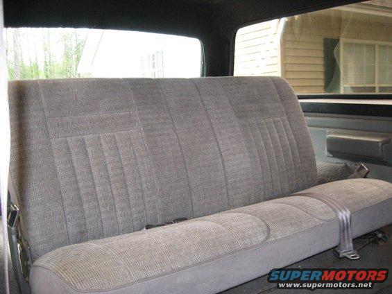 Back seat of a vehicle, gray fabric with vertical stitching pattern. Seatbelt visible