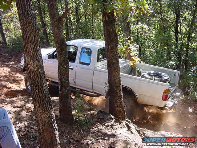 White pickup truck navigating a wooded trail, kicking up dust