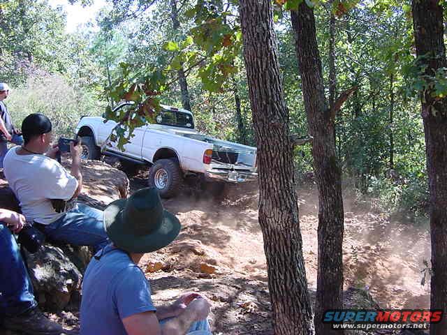 White pickup truck driving up a dirt hill with people watching
