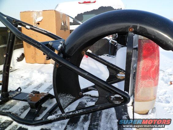 Black motorcycle frame and fender in a snowy truck bed with a cardboard box