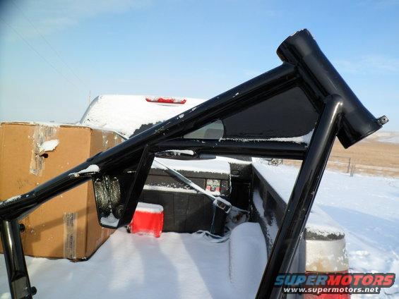 Black roll cage in the bed of a pickup truck covered in snow, with a large cardboard box and a red cooler also in the bed