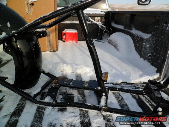 Motorcycle frame and fender in a snow-covered truck bed with a red gas can and boxes