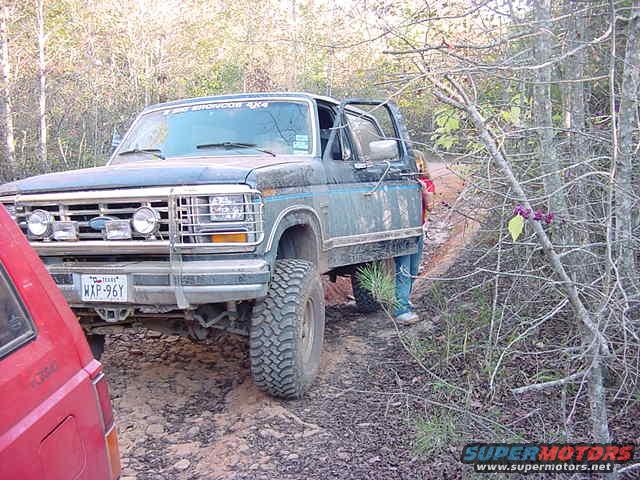 Blue Ford Bronco 4x4 on dirt road, front quarter view, dented bumper, open driver door