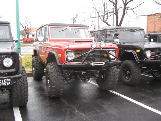 Red 1978 Ford Bronco with bull bar and large tires parked next to other Broncos