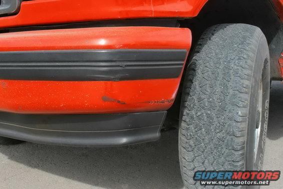 Close-up of an orange SUV's fender with black trim and a tire. Some scuffs on the fender