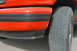 1995 Ford Bronco - The front corner of an orange SUV shows some wear and tear on the fender and bumper trim.