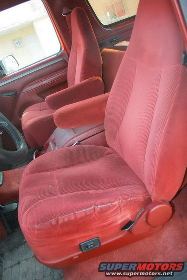 Red velour bucket seats with armrests inside a vehicle. Power seat controls visible on the side of the driver's seat