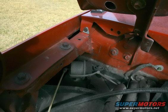Close-up of engine bay with red painted metal, bolts, wires, and a black hose