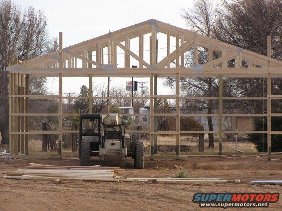 construction site with unfinished wooden building frame, two pieces of heavy machinery, and lumber piles