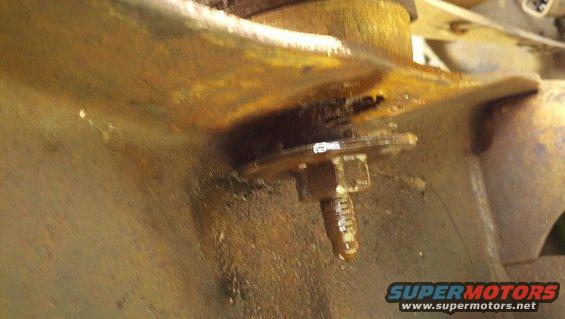 Close-up of a heavily rusted metal bracket with a bolt and washer, showing oil residue