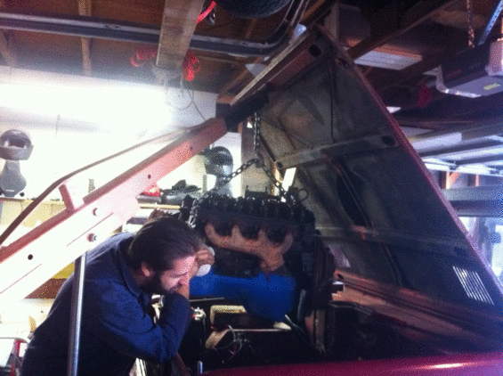 Mechanic working on vehicle underside, possibly an engine pull