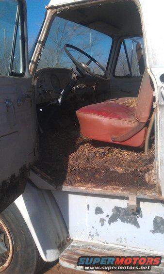 1973 Ford F-100 interior showing red seat, dashboard, steering wheel, and debris on the floor