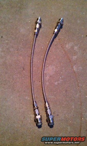 Two braided metal brake lines with silver fittings on concrete