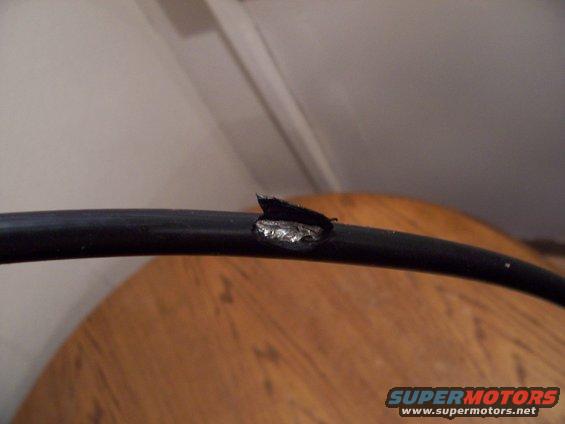 Close-up of a black cable with a damaged section showing exposed metal