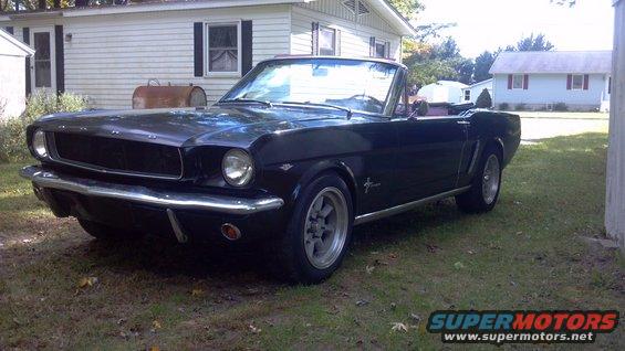 Black 1965 Ford Mustang convertible parked in a grassy yard next to a house