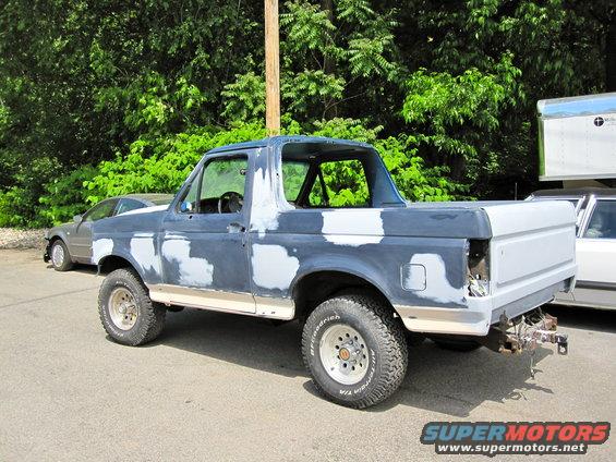 Blue Ford Bronco with primer patches, side view, undergoing repairs